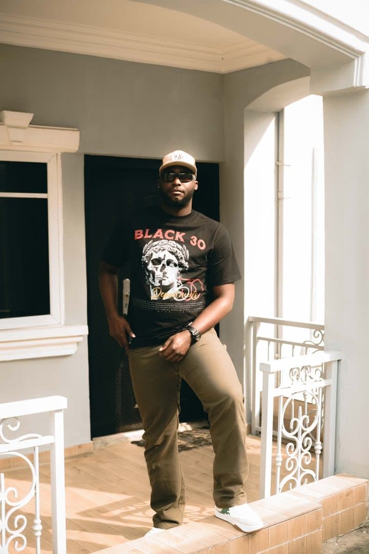Woriidem in sunglasses and a black graphic tee on a white porch
