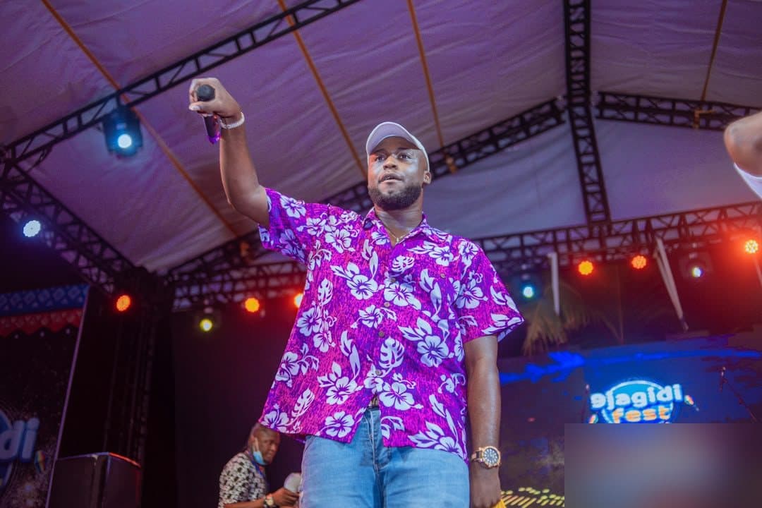 Woriidem on stage in a purple floral shirt, microphone raised to the crowd